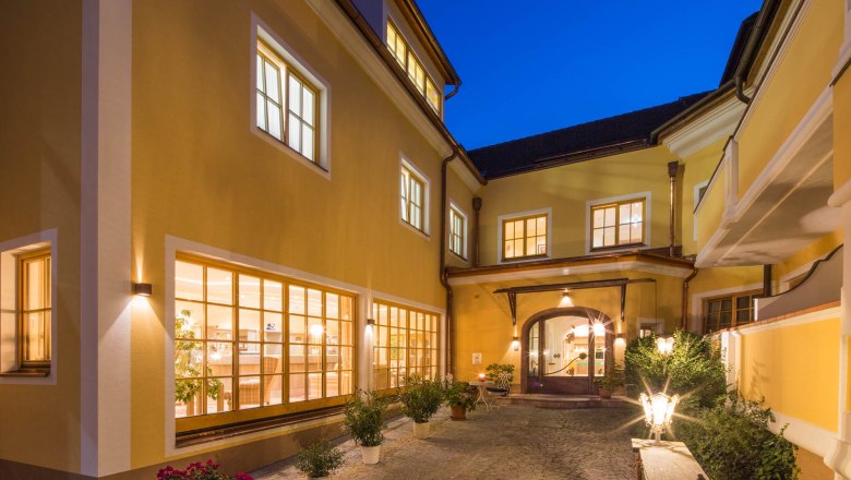 Hotel-Restaurant "Zum Schwarzen Bären", © Lachlan Blair Inner courtyard of the Hotel Zum Schwarzen Bären with illuminated windows and plants at night.