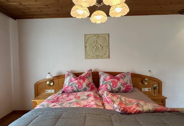 Bedroom upper floor, © Heidi Peer A cozy bedroom with a double bed, floral bedding and a wooden ceiling. A lamp hangs from the ceiling.