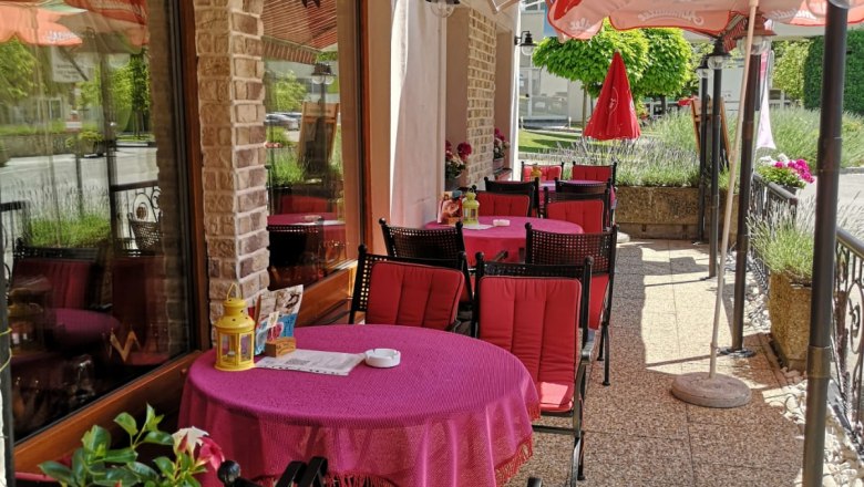 Cafe terrace, © Hotel- Kur-Kaffee-Konditorei & Restaurant "König Stefan" Outdoor terrace of a café with red tables and chairs under a striped awning.