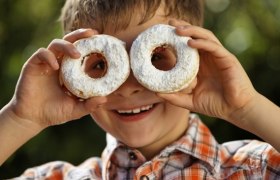 lucas, © SchaglOG A boy holds two doughnuts sprinkled with powdered sugar in front of his eyes.