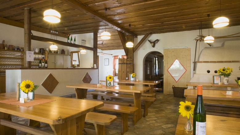 Wine tavern Buchecker, © Weingut Buchecker Interior view of a traditional wine tavern with wooden tables, sunflowers and bottles of wine.