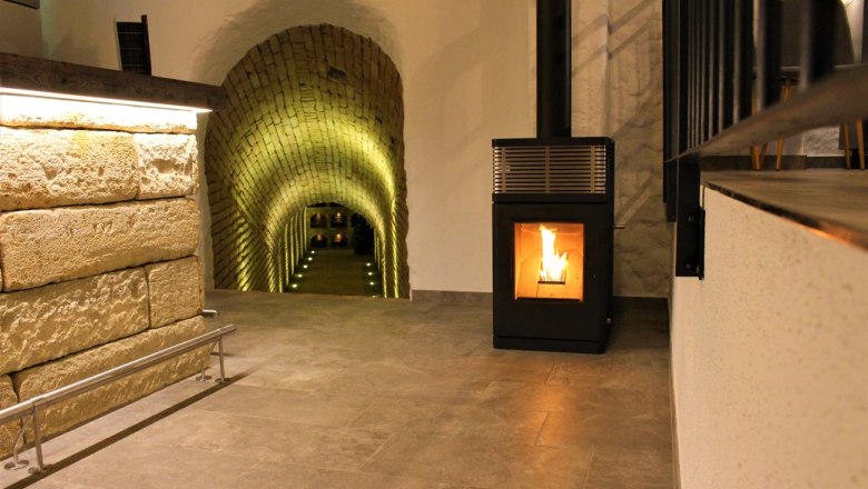 Wine shop, © Weingut Kerner A wine cellar with an illuminated vaulted corridor and a burning fireplace.