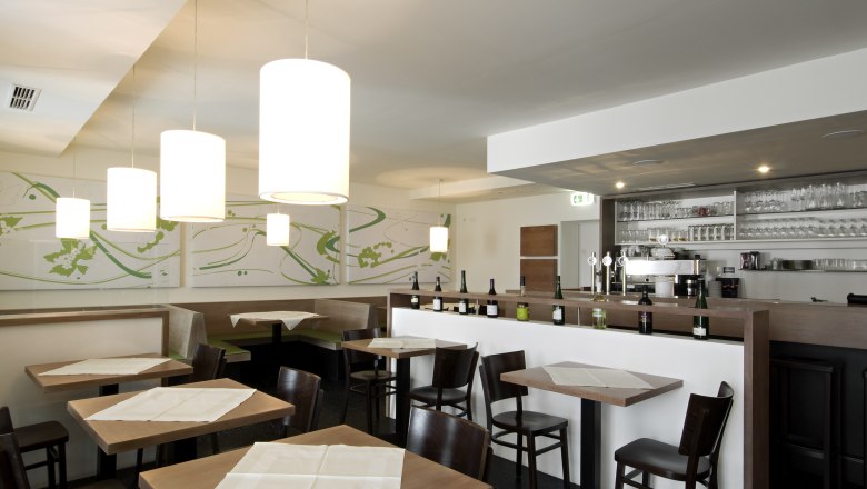 Restaurant Zur Schonenburg, © Gasthof Hotel "Zur Schonenburg" Interior view of a modern restaurant with wooden tables, chairs and a bar with bottles and glasses.