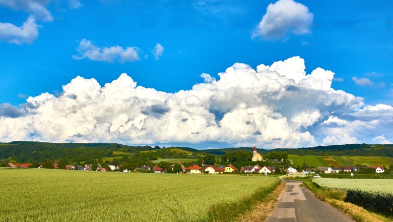 Woman village, © M. Greil Landscape with village, fields and church in front of large clouds.
