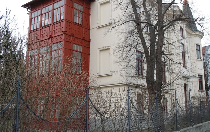 Schönberg House & Memorial Cane, © Schönberg Haus & Gedenkstock A historic building with a red bay window and a fence in the foreground.