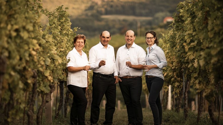 Family Winery Christoph Donabaum, © Nimo Zimmerhackl Four people stand smiling in a vineyard with wine glasses in their hands.