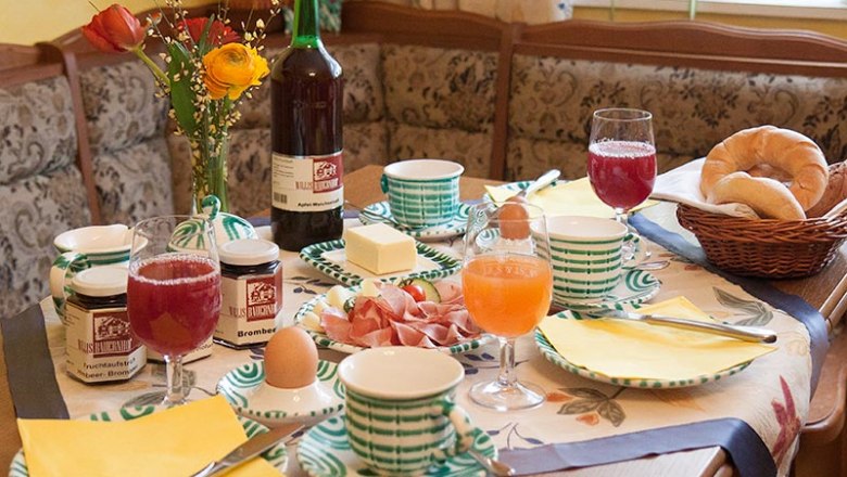Breakfast, © © Fam. Wilhelm A laid breakfast table with bread rolls, jam, eggs, juice and flowers.