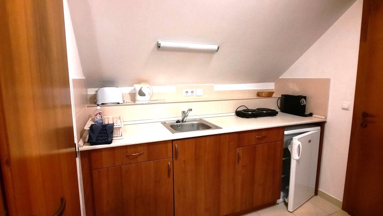 Kitchen unit, © Ildiko Davidne Nagy Small kitchenette with wooden cupboards, sink, toaster, kettle and mini-fridge under a sloping roof.