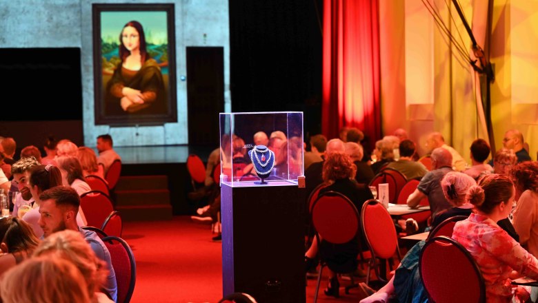 In-house production Kreuzverhör Papierfabrik Varieté, © Stefan Wasner A theater with people at tables, an illuminated piece of jewelry in a display case and a picture of the Mona Lisa in the background.