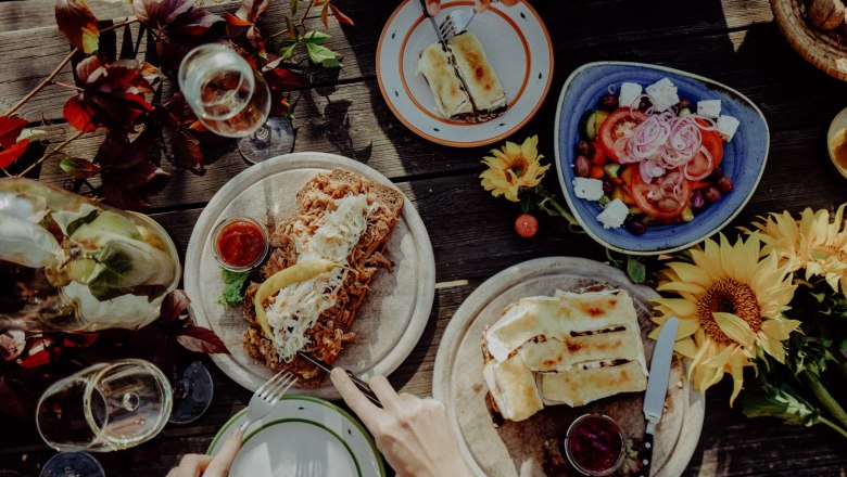 Excerpt from the menu, © Alter Klosterkeller A table with various dishes, including salad, bread with toppings and wine, decorated with sunflowers.