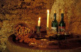 Wine cellar, © Günter Schneider A wine cellar with candlelight, two bottles of wine, glasses and a basket full of walnuts on a barrel.