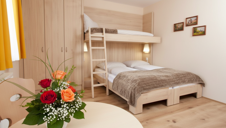 Triple room, © Austria-Best-Hotels A cozy hotel room with a double bed and a bunk bed, a wooden table with a bouquet of flowers and a closet.