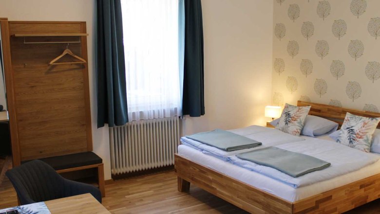 Double room, © Magdalena Donhauser Comfortable double room with bed, closet, table, chair and window with blue curtains.