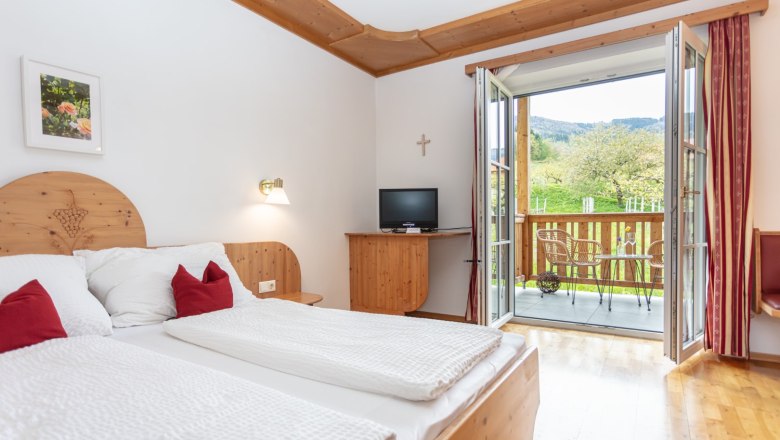 Double room with balcony, © Weingut Rixinger A cozy double room with wooden furniture, a balcony with a view of the countryside and a small TV.