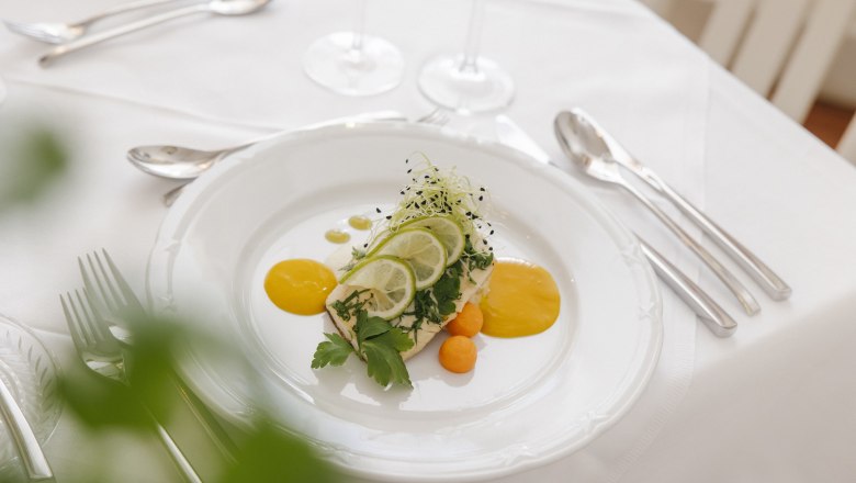 Gloggnitz Castle Restaurant, © Wiener Alpen/ Sophie Menegaldo Elegant dish on a white plate garnished with lime slices and herbs on a laid table