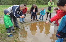 bird.show.places, © Nüsken Group of adults and children watching a puddle outdoors.