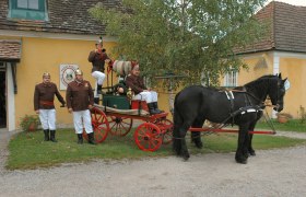 Lanzenkirchen Fire Brigade Museum, © Gemeinde Lanzenkirchen Historic fire engine with horse and firemen in uniform in front of a yellow building.