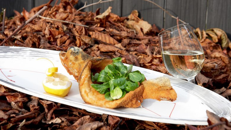 Fish, © A.Ch. Wulz Fried fish with lamb's lettuce and lemon on a plate, next to a glass of white wine, on a bed of autumn leaves.