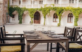 Guest garden in historic inner courtyard, © Niederösterreich Werbung/Daniela Führer A table set in a historic courtyard with vines on the walls.