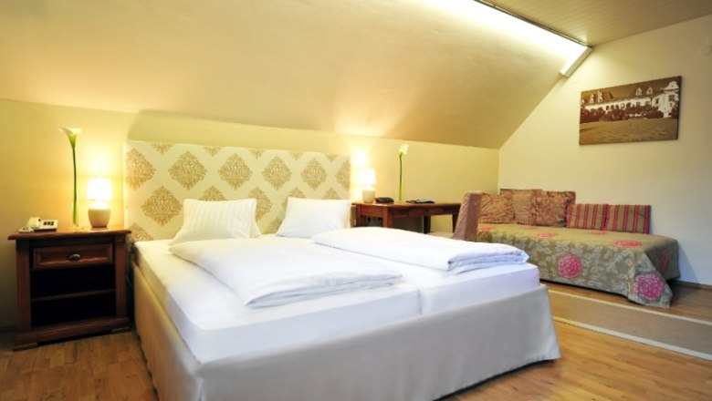 Renaissance Hotel Raffelsberger Hof, © Renaissancehotel “ Raffelsberger Hof “ Hotel room with double bed, sofa and wooden furniture.