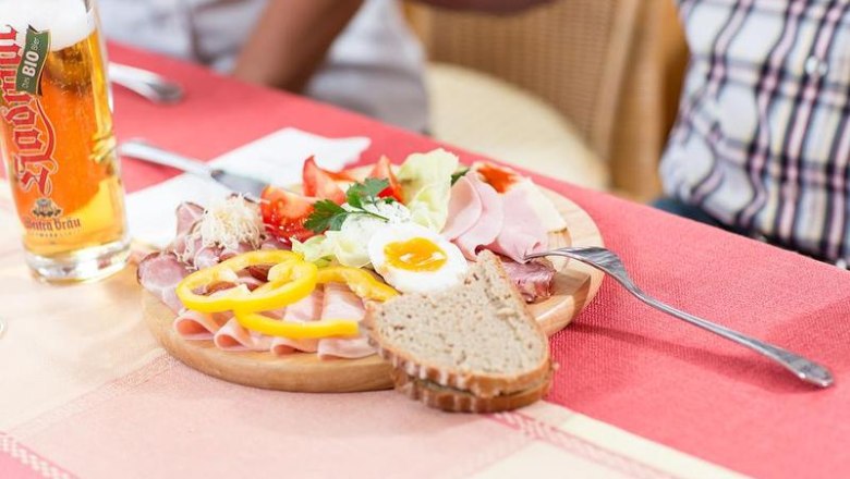 Enjoy Xund, © Café-Pension Kristall A plate of cold cuts, vegetables and egg on a table with a glass of beer next to it.