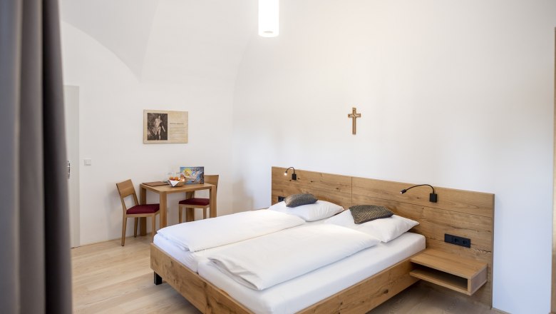 Göttweig Abbey, guest house, © Robert Herbst A simply furnished guest room with a double bed, wooden furniture and a cross on the wall.
