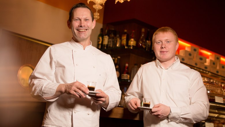 Cafe Helmut & Helmut, © schwarz-koenig.at Two men in a café holding espresso cups and smiling at the camera.
