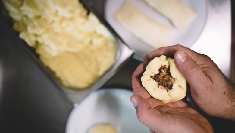 1st Wirtshausknödelmanufaktur ®, © Niederösterreich Werbung/Mara Hohla Hands form a filled dumpling from dough.