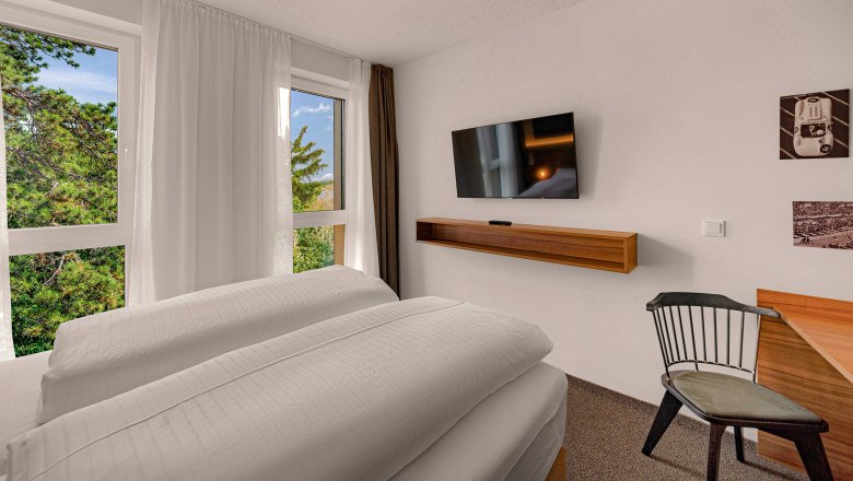 Zündwerk Motel, © propertyphotos.at Modern hotel room with large bed, flat screen TV, desk and chair. Window with view of trees.