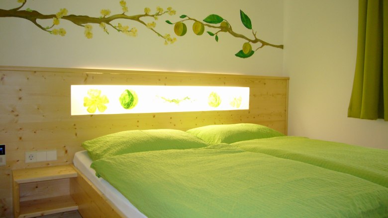 Creeper room - Gasthof zur Kirche, © Gasthof zur Kirche A cozy room with a double bed, green bed linen and a wall decoration with yellow flowers and fruits.