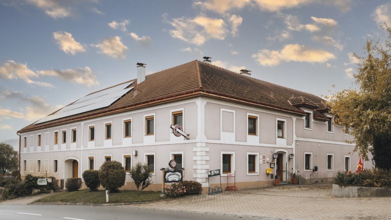Country inn in Kilb, © Niederösterreich Werbung/David Schreiber A traditional country inn with solar panels on the roof and a sign in front of the entrance, under a cloudy sky.