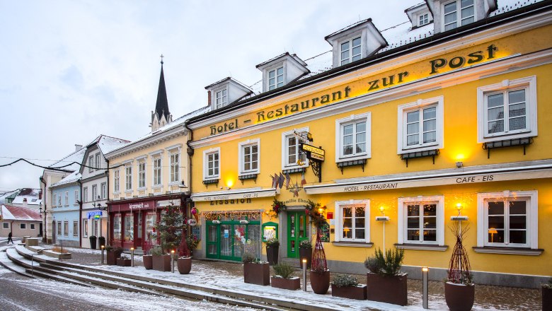 Exterior view in winter Hotel-Restaurant Zur Post, © Helmut Lackinger Exterior view of a yellow building with the inscription 'Hotel-Restaurant zur Post' in winter, surrounded by snow and decorated with lights.