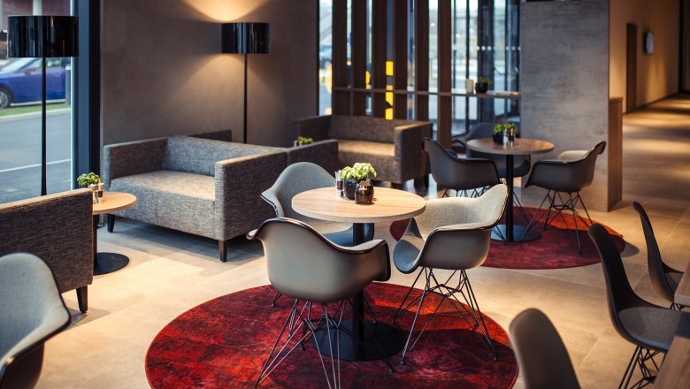 Hotel Rainers21, © Hotel Rainers21 Modern hotel lobby with gray sofas, round wooden tables and red carpets.