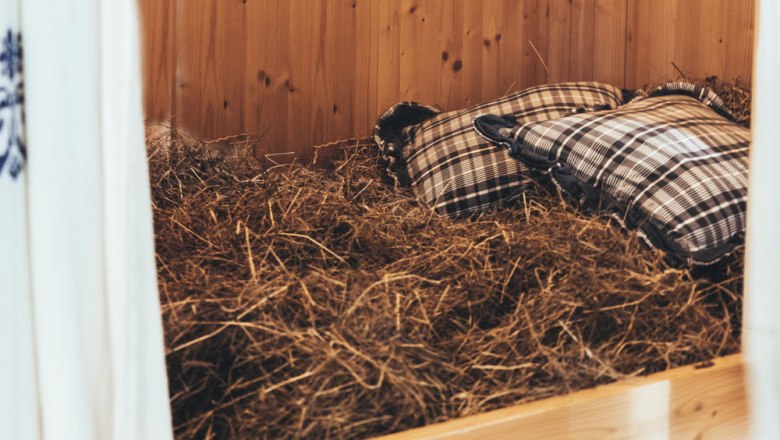 Wellness in a hay bed, © Niederösterreich Werbung/David Schreiber Hay bed with checkered pillows in a wooden room.