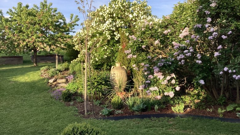 The garden as a place to relax, © Weitschacher A well-tended garden with flowering shrubs, a tree and a large vase in the sunlight.