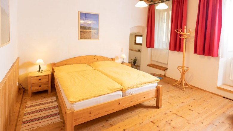 Bedroom, © Fam. Zangl Cozy bedroom with wooden furniture, yellow bed linen and red curtains.
