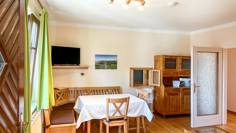 House Morning sun Dining room, © Fam. Pauker Dining room with wooden furniture, table with white tablecloth, green curtains and TV on the wall.