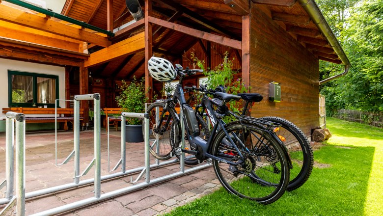 Hubertushof - bicycle parking lot, © Wiener Alpen/Martin Fülöp Bicycles in a bicycle rack in front of a wooden building with a terrace.