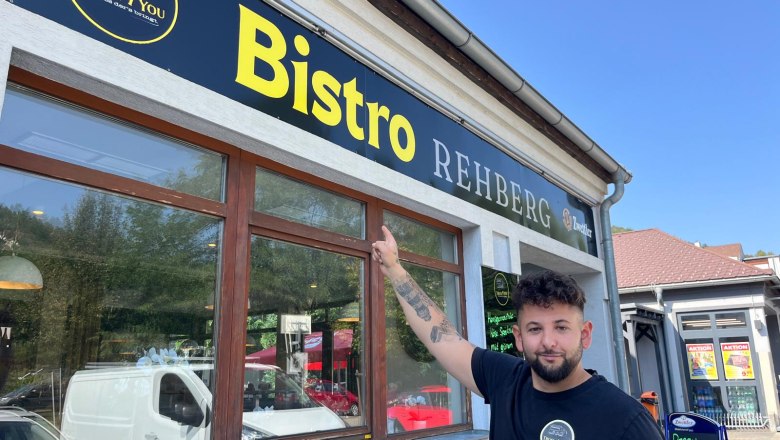 Bistro Rehberg, © Stadtmarketing Krems A man points to a sign saying 'Bistro Rehberg'.