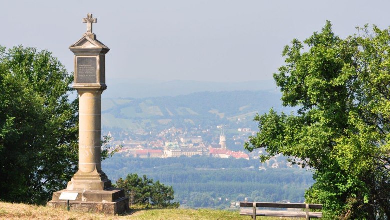 Bisamberg, © Gemeinde Bisamberg Column with cross on a hill, in the background a town and hills.