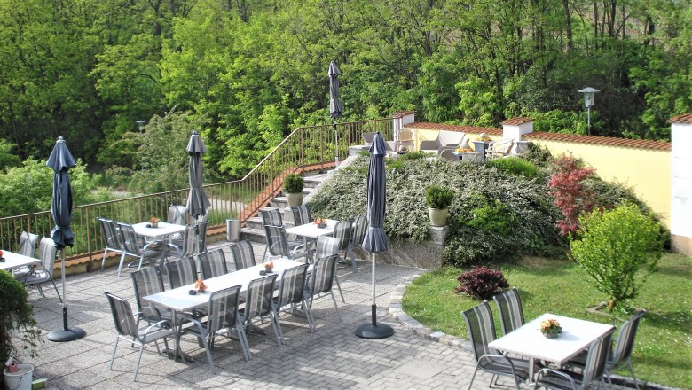 Guest terrace, © Pension Rudi Guest terrace with tables, chairs and parasols, surrounded by green vegetation.