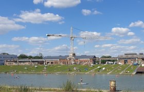 korneuburg-danube-werftbad-liegewiese, © SEFKO People relaxing on a lawn by a river with a crane in the background.