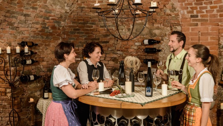 Wine cellar in the Hotel-Restaurant Zur Post, © BOW Rita Newman Four people in traditional dress are standing in a wine cellar holding wine glasses. They are laughing and chatting at a round table.