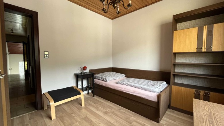 Vacation apartment by the river, © Roland Krätzel A simply furnished bedroom with single bed, wooden ceiling, shelf and small table with lamp.
