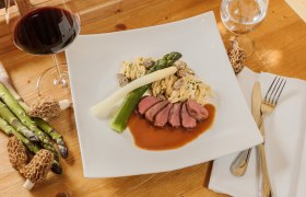 Emperor of Austria, © Rita Newman Gourmet dish with meat, asparagus, pasta and morels on a white plate, with a glass of red wine next to it.