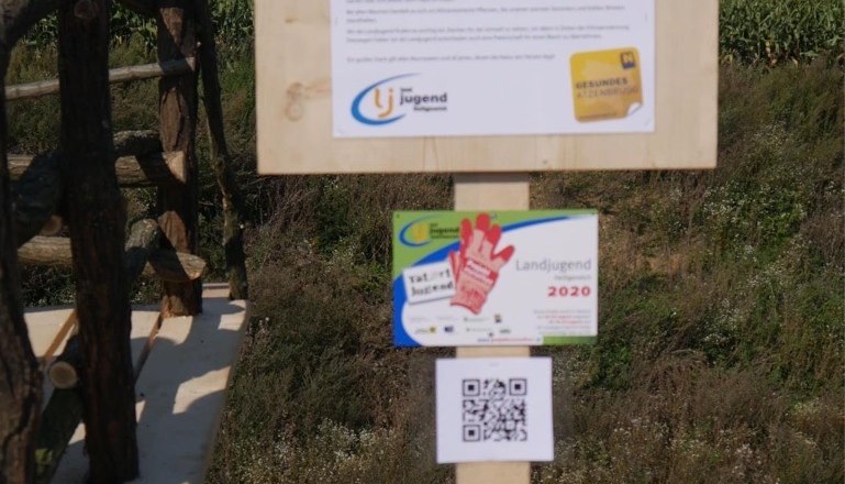 Tree nature trail-Atzenbrugg, © Landjugend Heiligeneich Wooden sign with information about the Atzenbrugg educational tree trail, surrounded by nature.