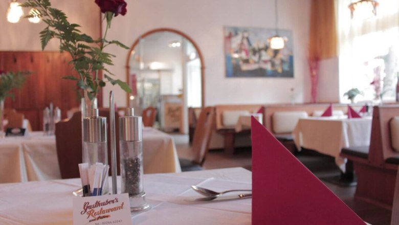 Restaurant Wirtshaus inside, set table with flower, © Gasthubers Wirtshaus Interior view of a cozy restaurant with laid tables, red napkins and a rose in a vase.