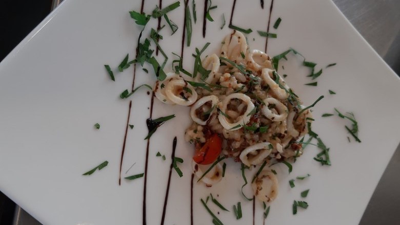 Calamari, © Reef & Beef A plate of decoratively arranged calamari, garnished with herbs and balsamic glaze.