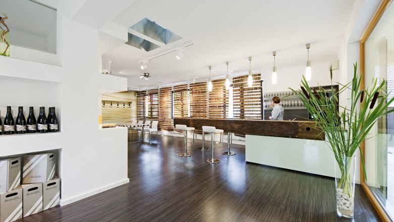 Tasting room, © Benedikt Modern tasting room with bar, chairs and wine bottles.