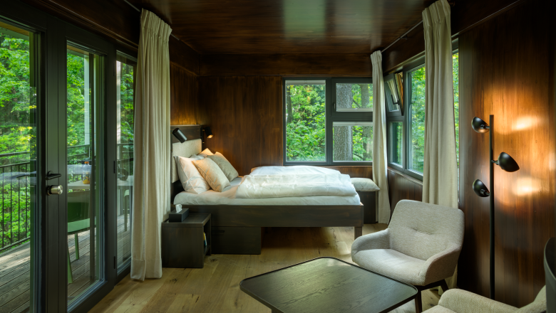 edelførst tree houses, © Robert Tober Interior view of a modern tree house with bed, armchairs and large windows with a view of the countryside.